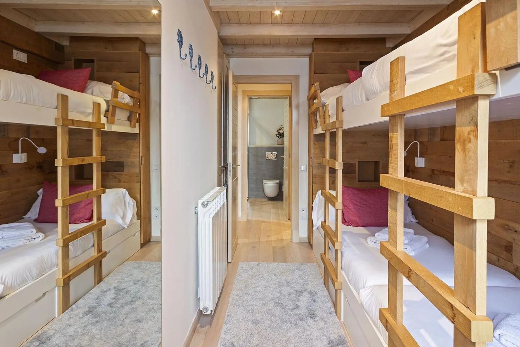 Un dormitorio con literas de madera, con el pasillo al fondo