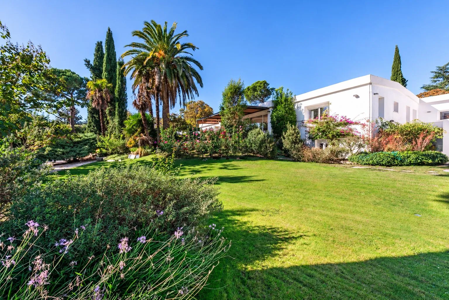 El jardín, con el césped, los parterres y la casa blanca al fondo