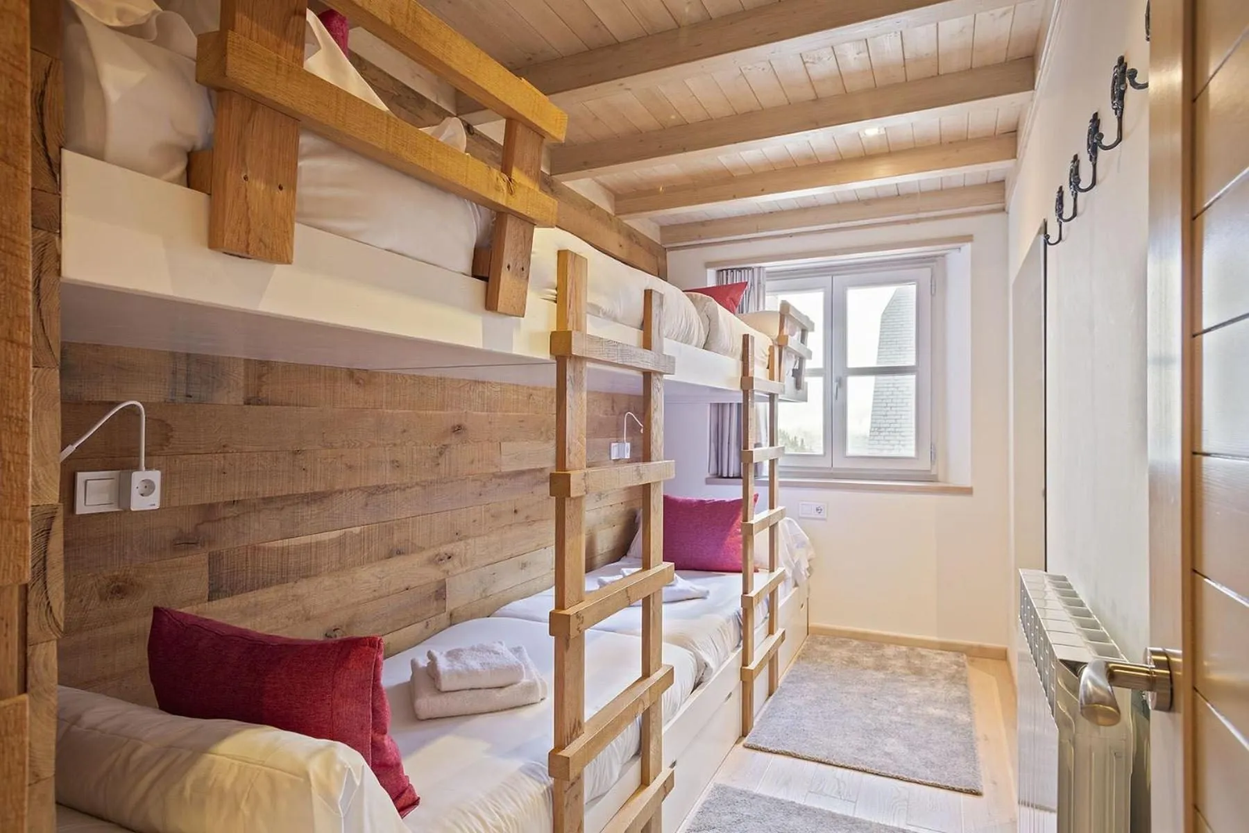 Las literas de madera, con cojines rojos y la ventana al fondo