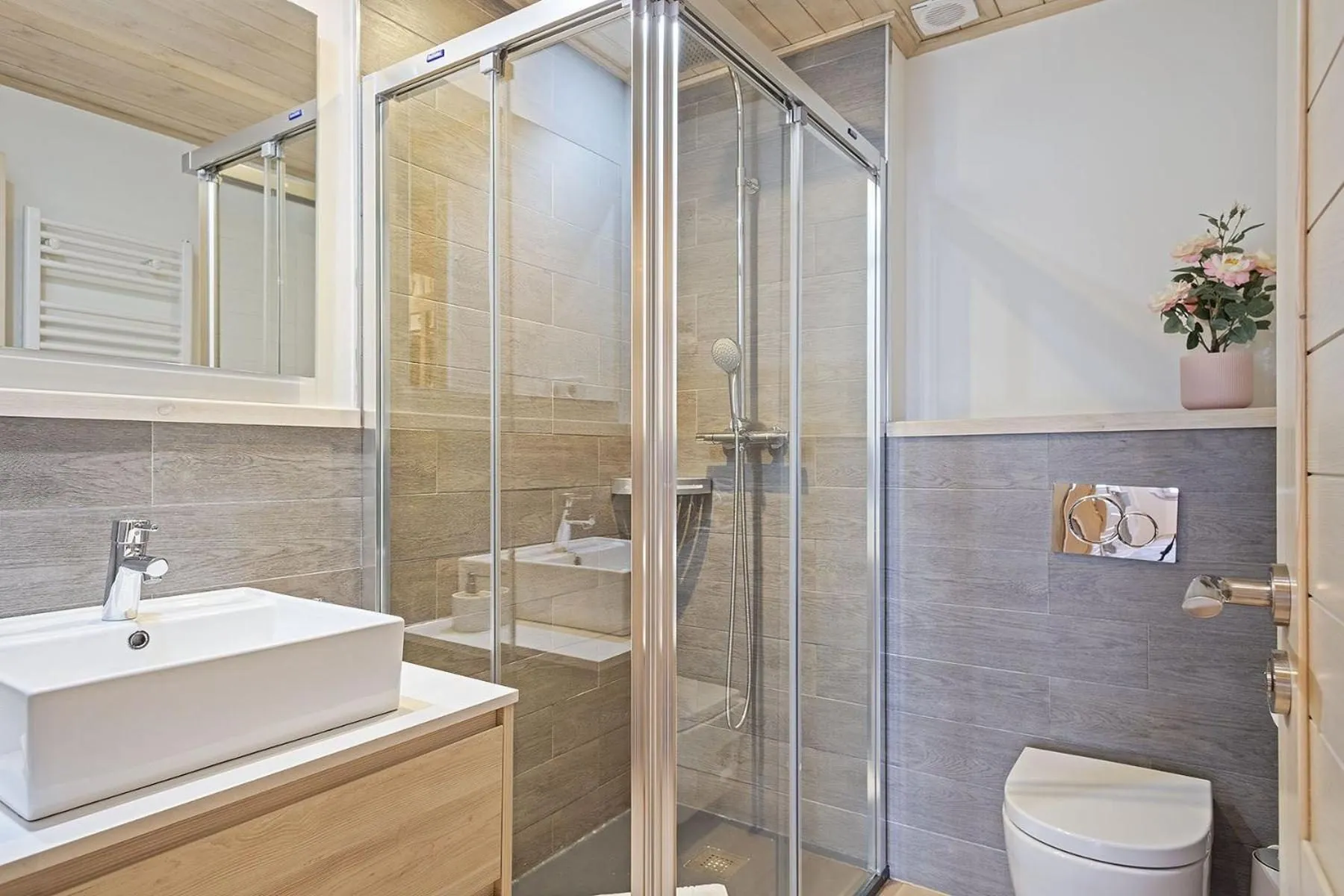 Un baño con ducha de cristal, lavabo blanco y pared de madera