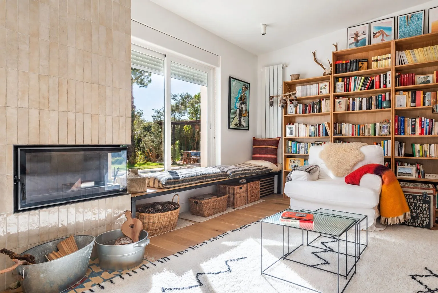 La chimenea empotrada en un muro de azulejo, con la librería y un banco bajo la ventana