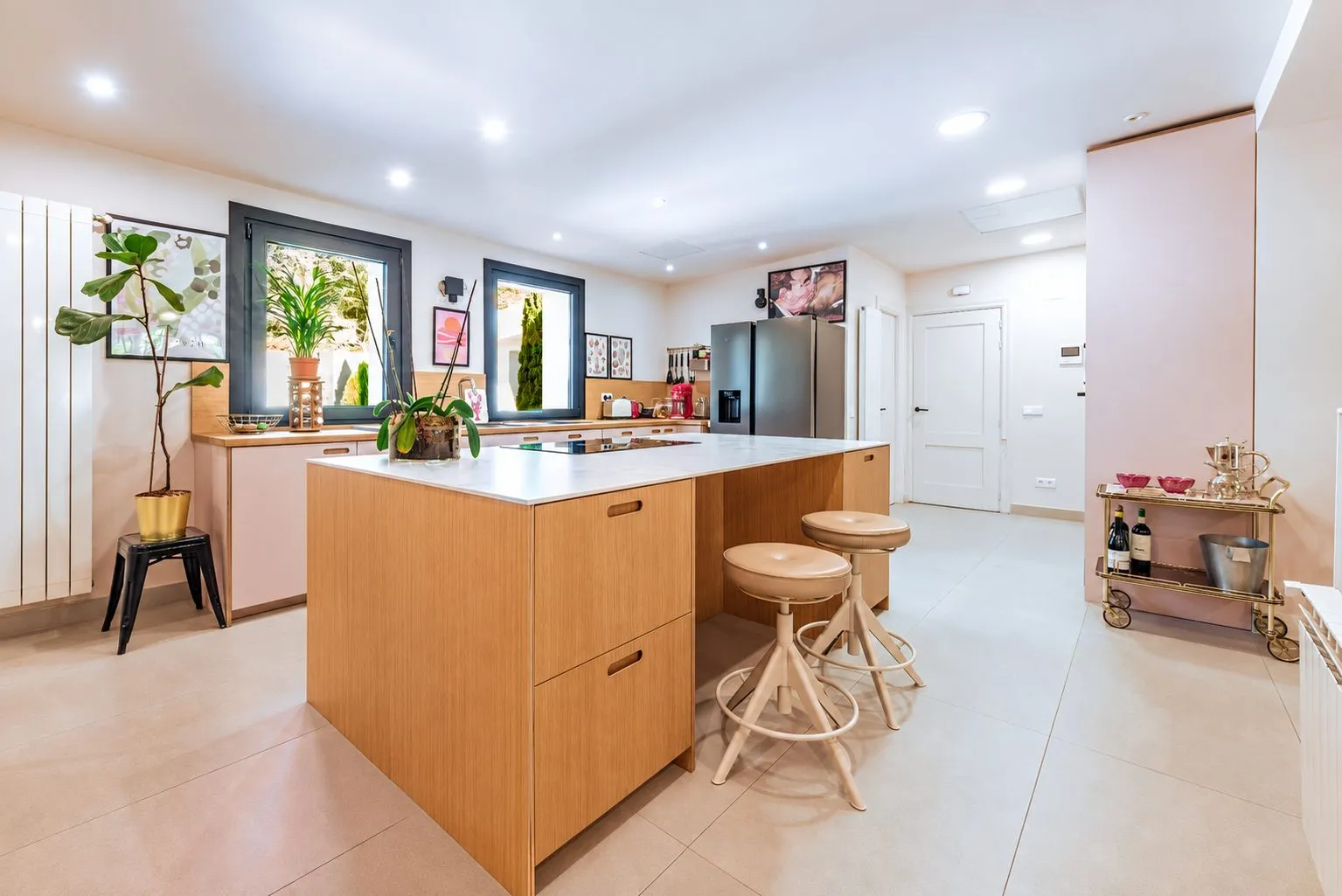 La cocina con isla de madera clara y taburetes