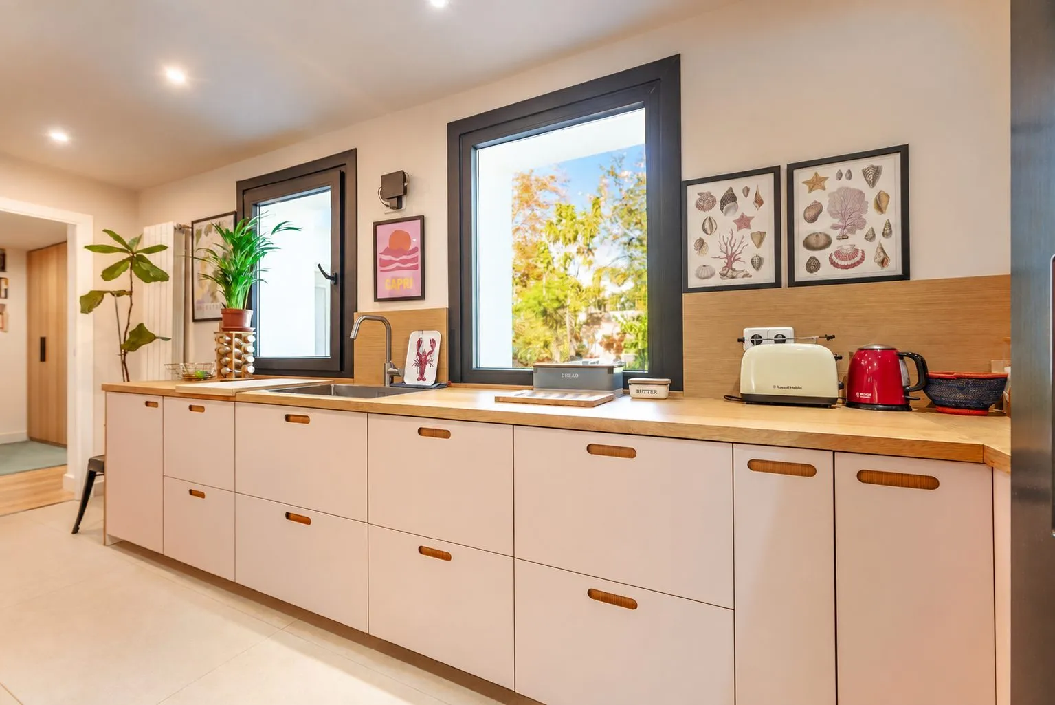 La cocina: muebles blancos con encimera de madera bajo dos ventanas