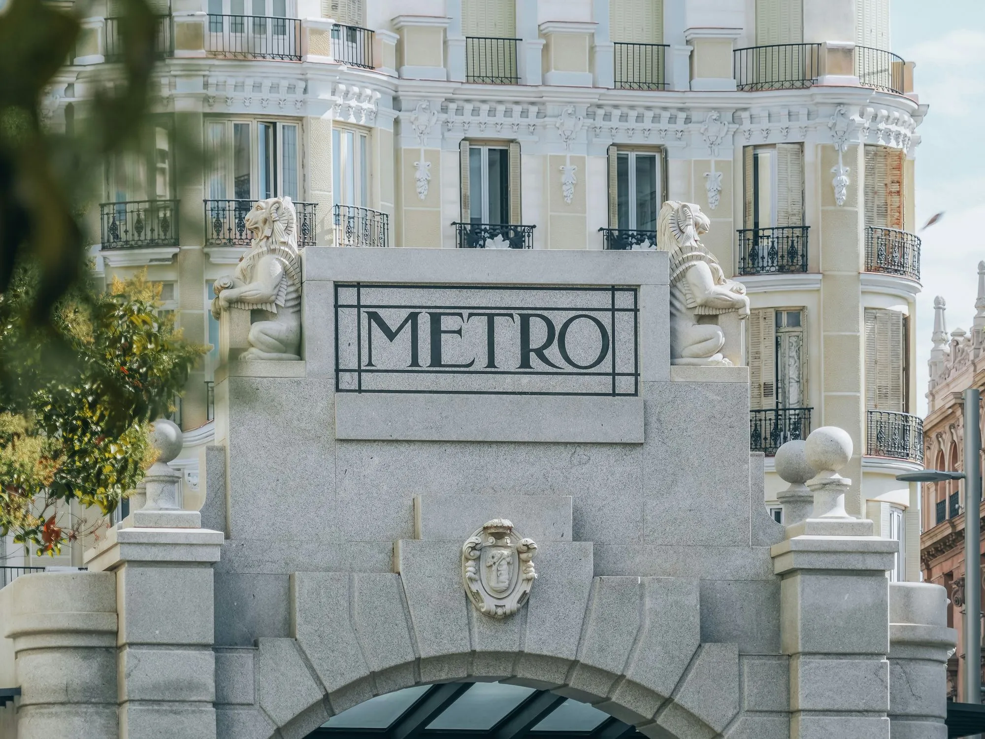El templete de piedra de una boca de metro con el rótulo METRO, delante de un edificio señorial con balcones de forja