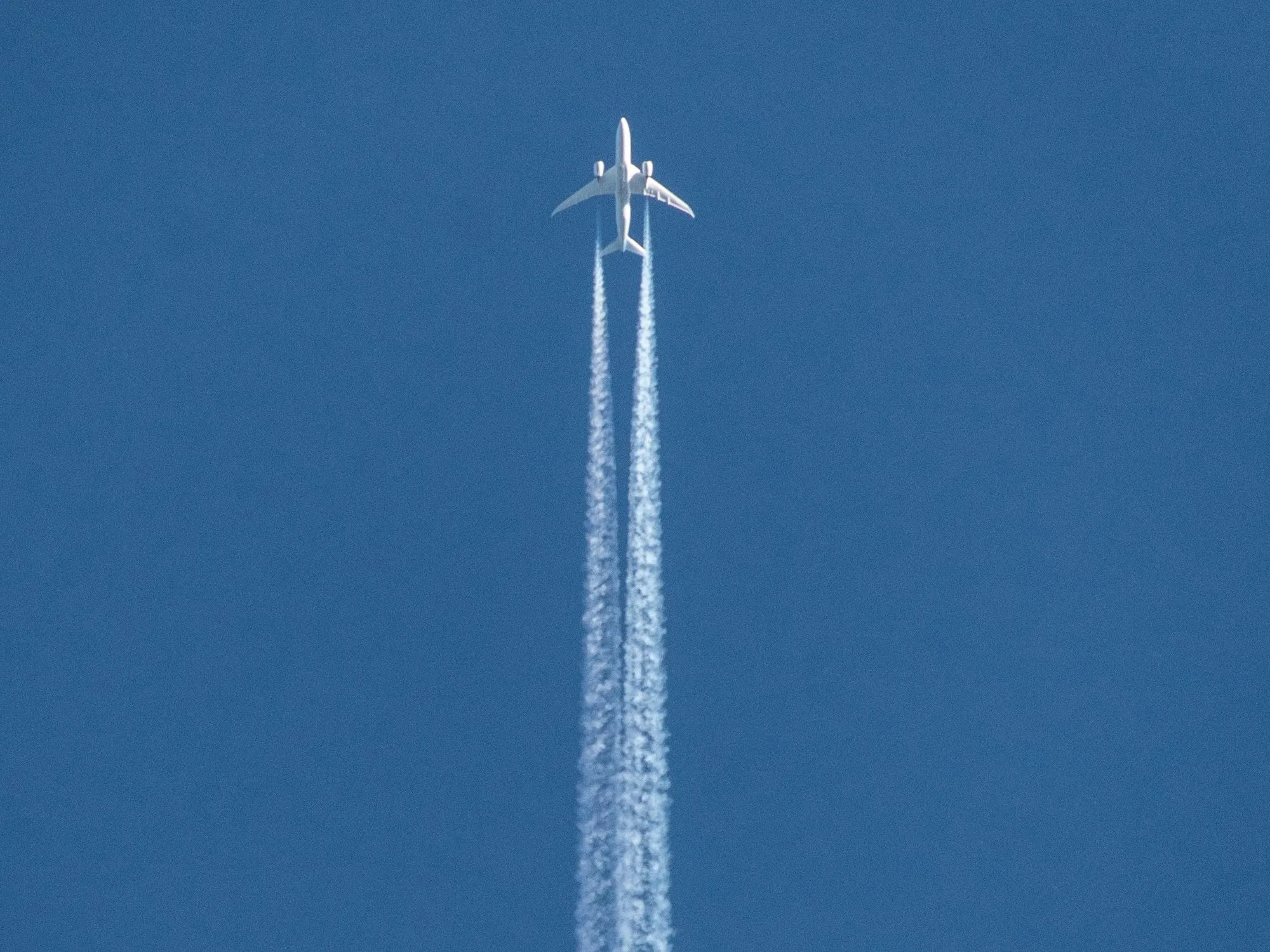 Un avión en lo alto de un cielo azul limpio, con su doble estela blanca
