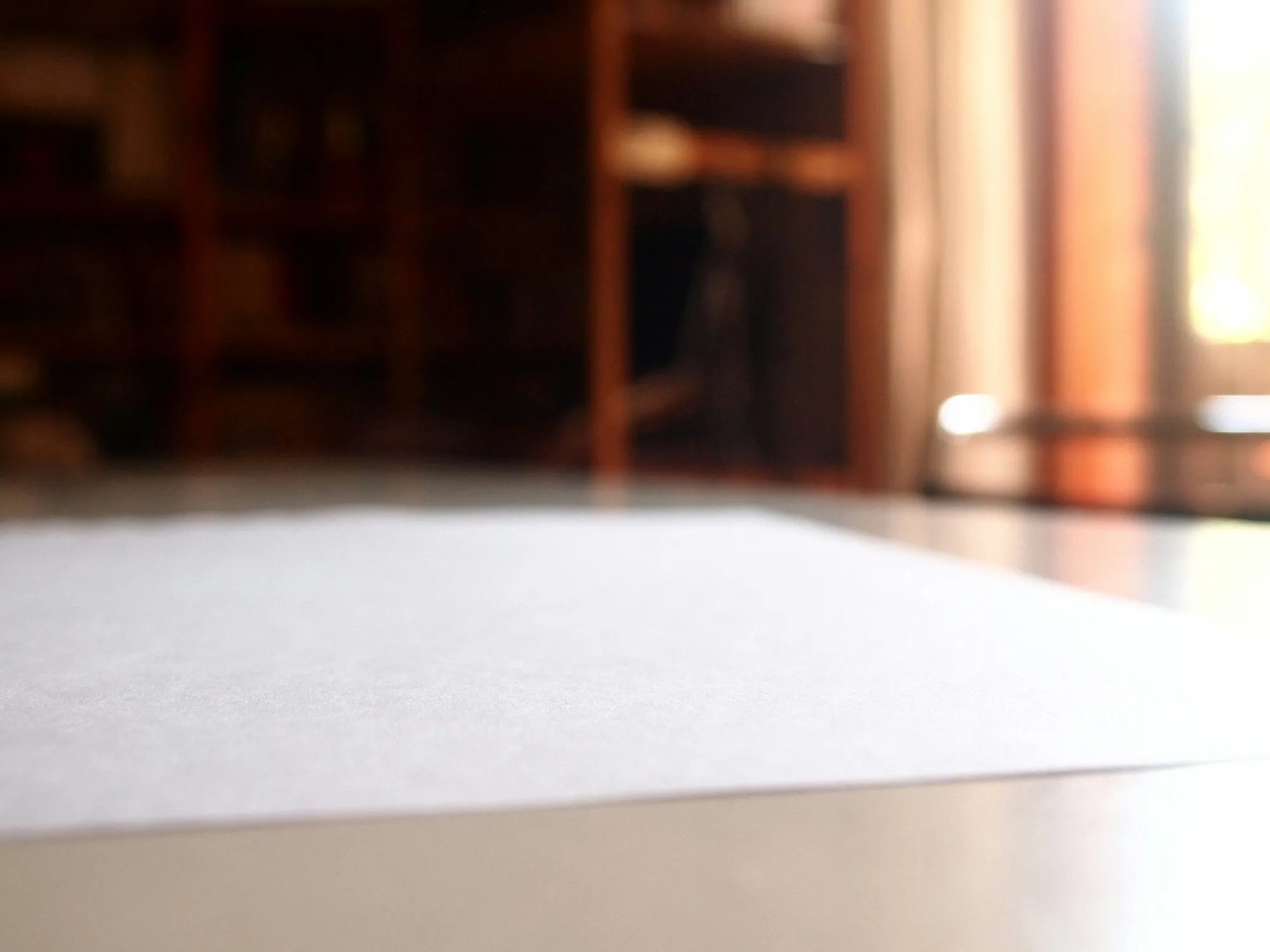 Una hoja de papel en blanco sobre una mesa de madera, con una estantería desenfocada al fondo